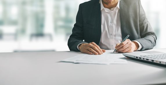 young man in suit writing business papers at desk in modern coworking office. copy space